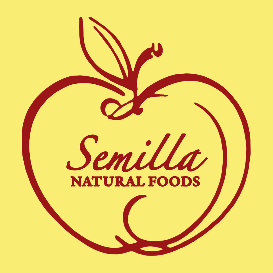 The image features the logo for "Semilla Natural Foods." The logo is a red outline of an apple, including a leaf and a stem, on a yellow background. The text "Semilla Natural Foods" is written in the center of the apple in red, cursive and capitalized font.